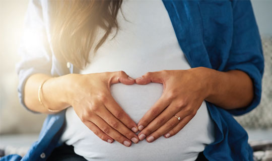 pregnant woman with her hands on her belly forming a heart